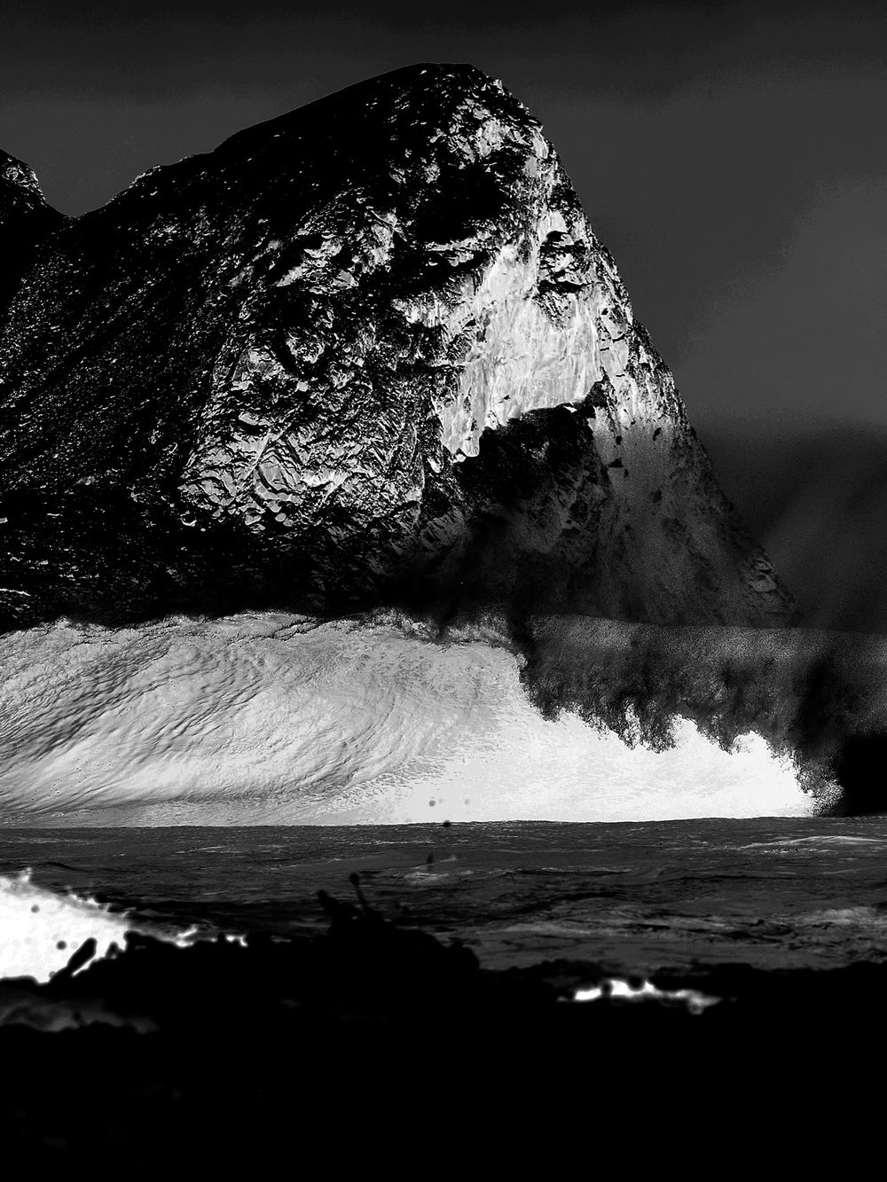 Dark mountain peak above a breaking wave, black and white