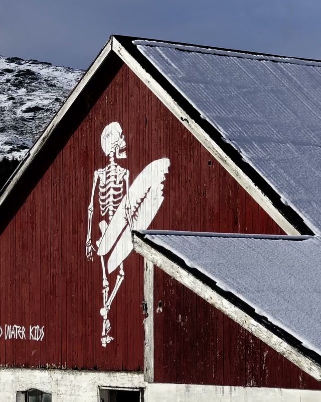 The CWK skeleton surfer painted on a red barn under snowy mountains