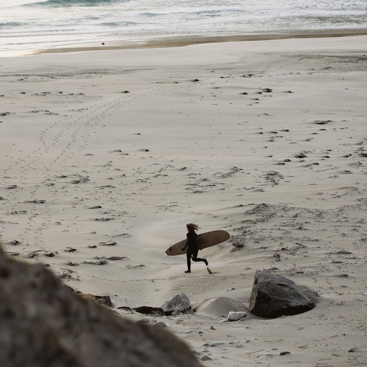 Surfer running along a wide beach with a board
