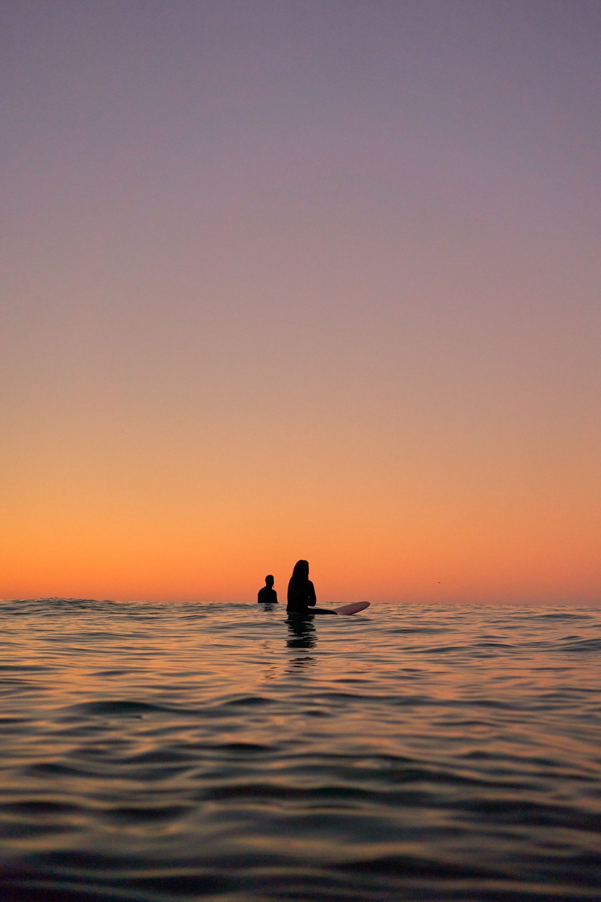 Two surfers waiting on their boards at sunset