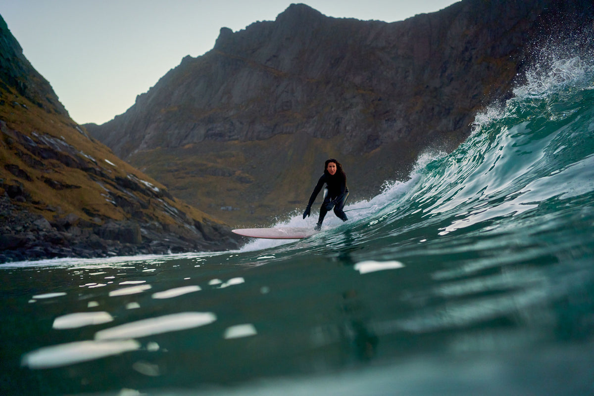 Surfer on a green wave below steep mountains
