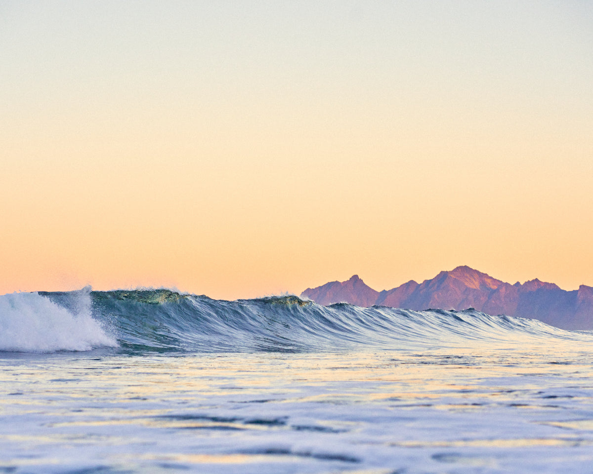 Wave breaking at dusk with snowy peaks on the horizon